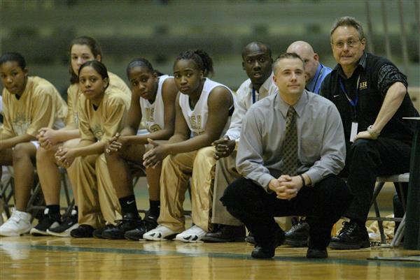 Coach Shepanski kneels in front of the girls basketball bench during a game